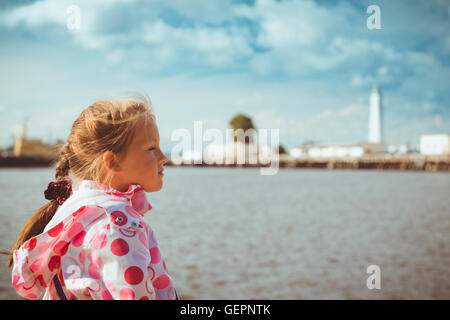 Mädchen in einem hellen rosa Jacke auf Grund der Blick von der Promenade auf dem Pier mit einem Leuchtturm und Schiffe in Kronstadt Stockfoto