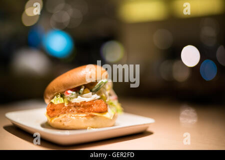 Gebratener Fisch-Burger mit Gemüse und Käse, Scheinwerferlicht, Bokeh dunklen Hintergrund weichzeichnen Stockfoto