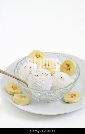Vanilleeis mit Bananenscheiben in einer Schüssel auf weißen Teller, Nahaufnahme, Makro, weißer Hintergrund Stockfoto