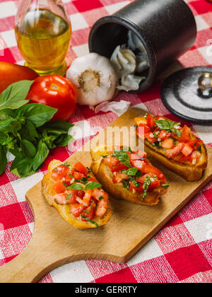 Foto von italienischen Bruschetta auf einem Holzbrett mit den Zutaten hinter. Konzentrieren Sie sich in der Mitte. Stockfoto