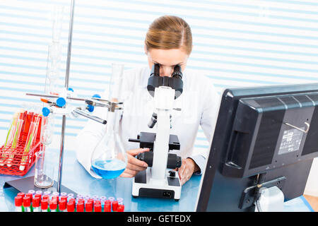 Frau in eine medizinische Laborantin mit einem Mikroskop und einem monitor Stockfoto