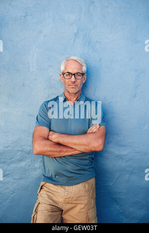 Vertikale Porträt zuversichtlich reifer Mann steht vor einem blauen Hintergrund. Kaukasischen Mann stehend mit Hallo Gläser Stockfoto