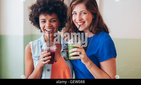 Porträt von zwei jungen Freunden trinken Saft aus frischen Früchten. Gemischte Rassen Frauen stehen zusammen mit Saft. Stockfoto