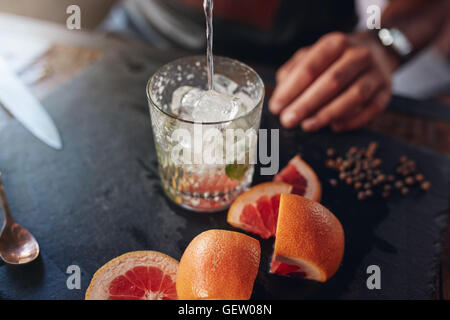 Closeup Aufnahme des Barkeeper Gießen Getränk in ein Glas voller Eiswürfel mit geschnittenen Grapefruits und Pfeffer auf Zähler. Vorbereitung Stockfoto
