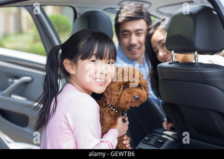 Glückliche junge chinesische Familie mit ihrem Hund im Auto sitzen Stockfoto