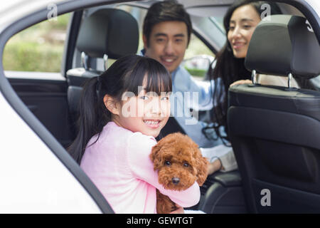 Glückliche junge chinesische Familie mit ihrem Hund im Auto sitzen Stockfoto