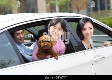 Glückliche junge chinesische Familie mit ihrem Hund im Auto sitzen Stockfoto