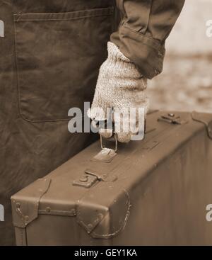 Einwanderer mit alten Leder Koffer und der gebrochenen Handschuh unterwegs Jobs im Ausland Stockfoto