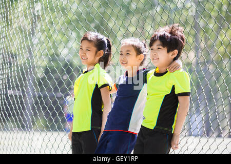 Glückliche chinesische Kinder Sportbekleidung gelehnt Maschendrahtzaun Stockfoto