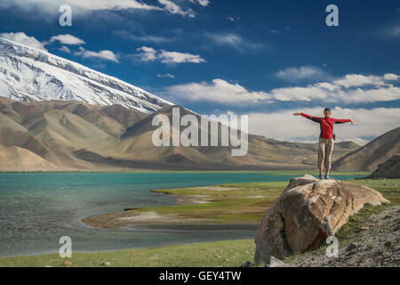 Frau steht auf einem riesigen Felsen am Ufer des Kara-Kul-See im Karakorum-Gebirge, Xinjang Provinz in China Stockfoto