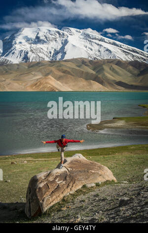 Frau steht auf einem riesigen Felsen am Ufer des Kara-Kul-See im Karakorum-Gebirge, Xinjang Provinz in China Stockfoto