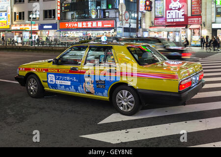 Ein gelbes Taxi warten in der Nacht für die Gäste auf einer belebten Straße im Stadtteil Shinjukunishiguchi in Tokio Stockfoto