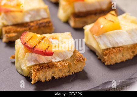 Kanapees, gegrillte Vorspeise mit Brie und Nektarine auf einer Schiefertafel Schale vergoldet Stockfoto