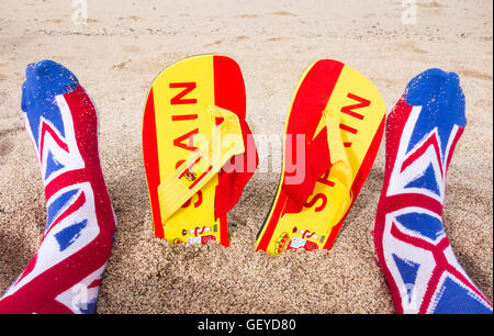 Britischer Tourist mit Union Jack Socken am Strand: Flip Flops mit spanischer Flagge im Sand. Brexit, Reisebeschränkungen, Freizügigkeit, EU Stockfoto