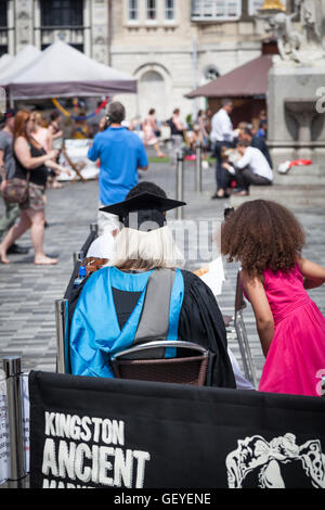 Absolvent trug einen Doktorhut und Kleid sitzt mit dem Rücken zur Kamera in einem Straßencafé. Stockfoto