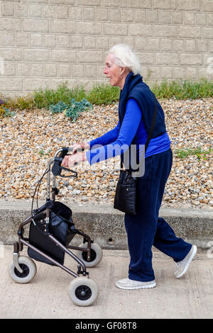 Eine ältere Frau zu Fuß mit einem Rollator zu Fuß Hilfe, Rottingdean, Sussex, UK Stockfoto