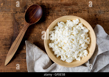 Hüttenkäse (Bauern Käse) in Holzschale, Holzlöffel, Textile auf rustikalen Holztisch. Draufsicht auf das Essen. Gesunde Ernährung Stockfoto