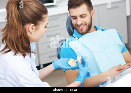 Schuss von einer Zahnärztin, jungen männlichen Patienten erklären, wie man seine Zähne richtig putzen. Stockfoto