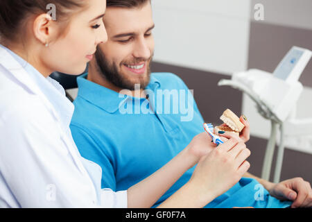 Schuss von einer Zahnärztin, jungen männlichen Patienten erklären, wie man seine Zähne richtig putzen. Stockfoto