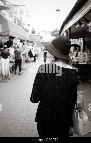 Rückseite einer jungen Dame / Teenager Mädchen auf gefliesten Straße Markt hält eine smart Tasche und einen schwarzen Hut Stockfoto