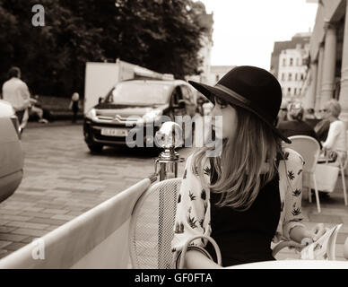 Junge 12 Jahre altes Mädchen Fedora Hut und Blick auf die Seite auf natürliche Weise. Am Tisch in einem Straße Seite Café sitzen. Stockfoto