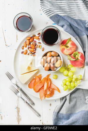 Wein snack Set. Käse, Hähnchen Carpaccio, mediterranen Oliven, Obst, Nüssen und zwei Gläser Rot auf Keramikplatte über weißem lackiertem Holz Hintergrund Stockfoto