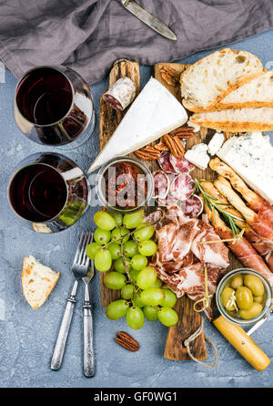 Käse und Fleisch Vorspeise Auswahl oder Wein Snack festgelegt. Vielzahl von Käse, Salami, Schinken, Brot-Sticks, Baguette, Honig, Trauben, Oliven, getrockneten Tomaten, Pecan-Nüssen über grauem Beton texturiert Kulisse, Ansicht von oben. Stockfoto