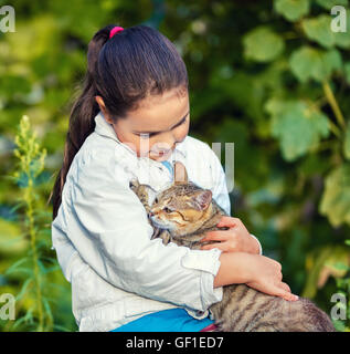 Trauriges kleines Mädchen umarmt eine streunende Katze im park Stockfoto