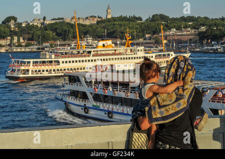 Eine Frau und Kind Uhr Fähren am Goldenen Horn, von Galata-Brücke.  Topkapi-Palast zu sehen in der Ferne über th Stockfoto