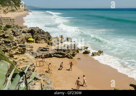 Junge Männer spielen Fußball auf einem Strand in der kleinen Küstenstadt von Los Caños de Meca, in der Provinz Cádiz. Einige Surfer warten auf Welle Stockfoto