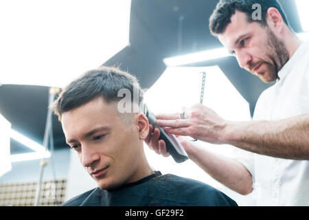 Professionelles Styling. Seitenansicht des jungen Mannes immer Haarschnitt von Friseur mit Elektrorasierer bei Barbershop hautnah Stockfoto