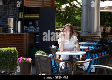 Glücklich Brünette Frau anrufen per Telefon im Open-Air-café Stockfoto