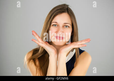 Überraschte Frau mit geöffneten Mund und großen Augen, die Hand in Hand im Gesichts und auf der Suche nach glücklich auf grauem Hintergrund isoliert Stockfoto