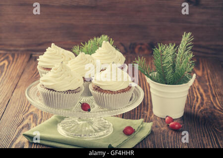 Hausgemachte Weihnachts Cupcakes mit Frischkäse Zuckerguss auf dem Kuchen stehen auf hölzernen Hintergrund mit Fichte Zweige in Keramik Eimer Stockfoto