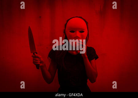 Geheimnisvolle Frau im schwarzen Kleid mit weißen Maske mit Messer, beängstigend Hintergrund für halloween Stockfoto