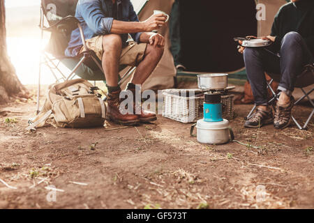 Zugeschnittenes Bild von ein paar sitzt vor dem Zelt und Kaffeezubereitung auf einem Campingkocher. Stockfoto