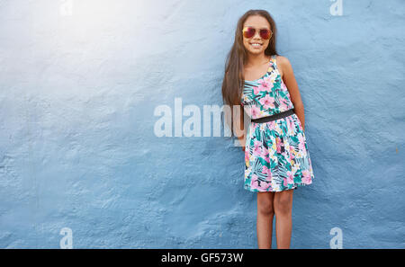 Porträt von entzückenden kleinen Mädchen in schönen Kleid und eine Sonnenbrille gegen blaue Wand mit Textfreiraum. Stockfoto