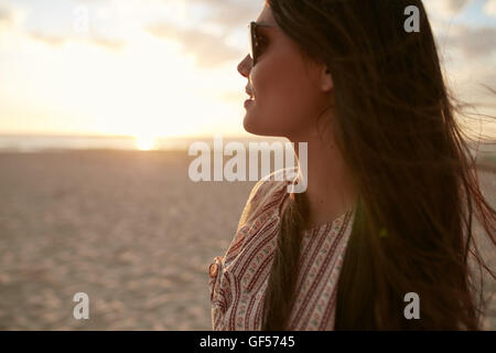 Schuss von schöne junge Frau mit Sonnenbrille entfernt betrachten hautnah. Kaukasische weibliches Modell am Meer bei Sonnenuntergang Stockfoto