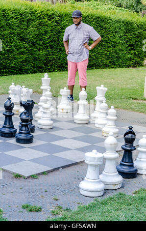 Ein Kerl spielen Sie eine Partie Schach auf dem riesigen Schachbrett in Holland Park, London. Stockfoto