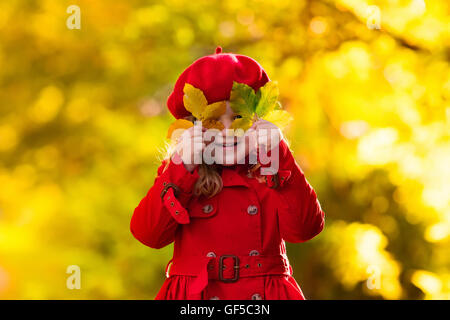 Glückliche kleine Mädchen in roten Barett und Trenchcoat spielen im schönen Herbst Park an warmen sonnigen Herbsttag. Stockfoto