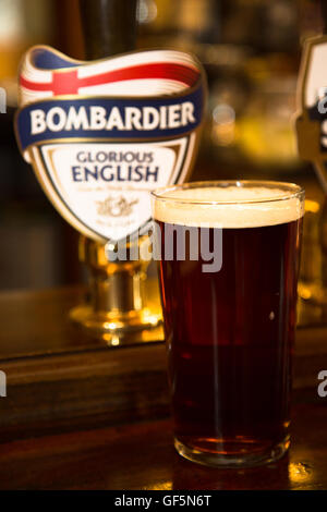 Abstrakte Sicht auf eine volle Pint englische Bombardier Ale/Bier neben den Pumphebel mit Pumpe Clips, aufgenommen in Durham, England. Stockfoto