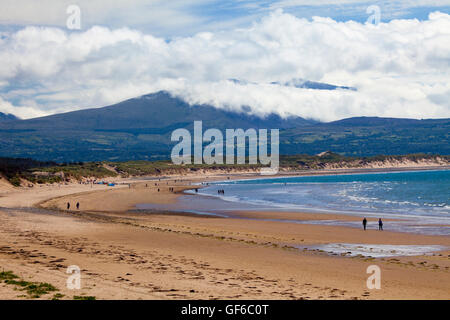 Menschen wandern entlang Newborough Strand mit Newborough Warren entlang der Sanddünen und Snowdonia-Nationalpark in der Ferne Stockfoto