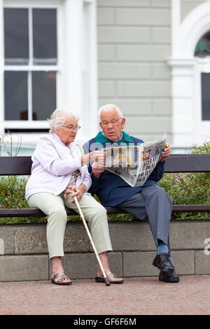 Älteres Ehepaar genießen gemeinsam die Zeitung lesen, während des Besuchs der Promenade an der Küste Stadt Llandudno, Wales, UK Stockfoto
