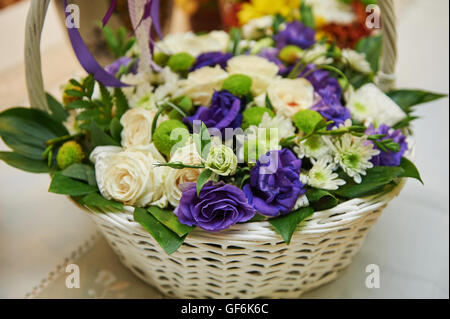 schöner Blumenstrauß weiße und violette Blumen im Korb auf Holztisch Stockfoto