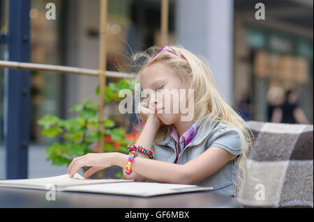 Entzückenden Kind Menü im Café lesen. Kleinkind müde Mädchen in wunderschöne Außen Café Speisekarte Essen auswählen. Stockfoto