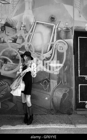 Monochrom von jungen Mädchen in kurzen Rock und Hut vor Graffiti mit Einkaufstüten wartet auf jemanden sieht cool Stockfoto