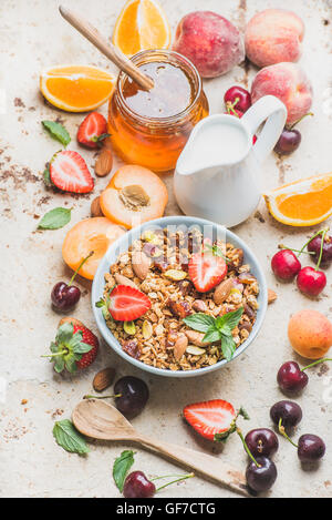 Gesundes Frühstückszutaten. Hafer-Müsli mit Nüssen, Erdbeeren und Minze in Schüssel geben, Milch in der Kanne, Honig im Glas, frisches Obst, Beeren auf konkrete Hintergrund Stockfoto