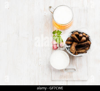 Bier-Snack-Set. Pint Pilsener im Becher und Roggenbrot Croûtons mit Knoblauch-Frischkäse-Sauce über weiß lackiert alten hölzernen Hintergrund Stockfoto