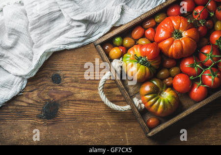 Bunte Tomaten in verschiedenen Größen und Arten in dunklen Holztablett über rustikale Hintergrund, Textfreiraum Stockfoto