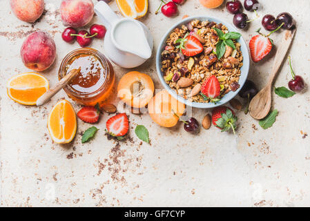 Gesundes Frühstückszutaten. Hafer-Müsli in Schale mit Nüssen, Erdbeeren und Minze Blätter, Milch in der Kanne, Honig im Glas, frisches Obst, Beeren auf konkreten Hintergrund, Textfreiraum Stockfoto